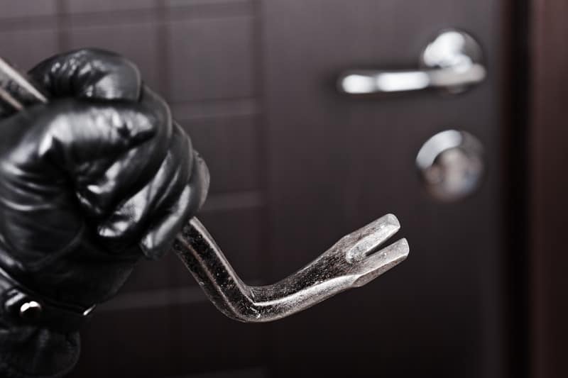 Black gloved hand with a crowbar in front of a locked door symbolizing the need to hire a qualified criminal lawyer